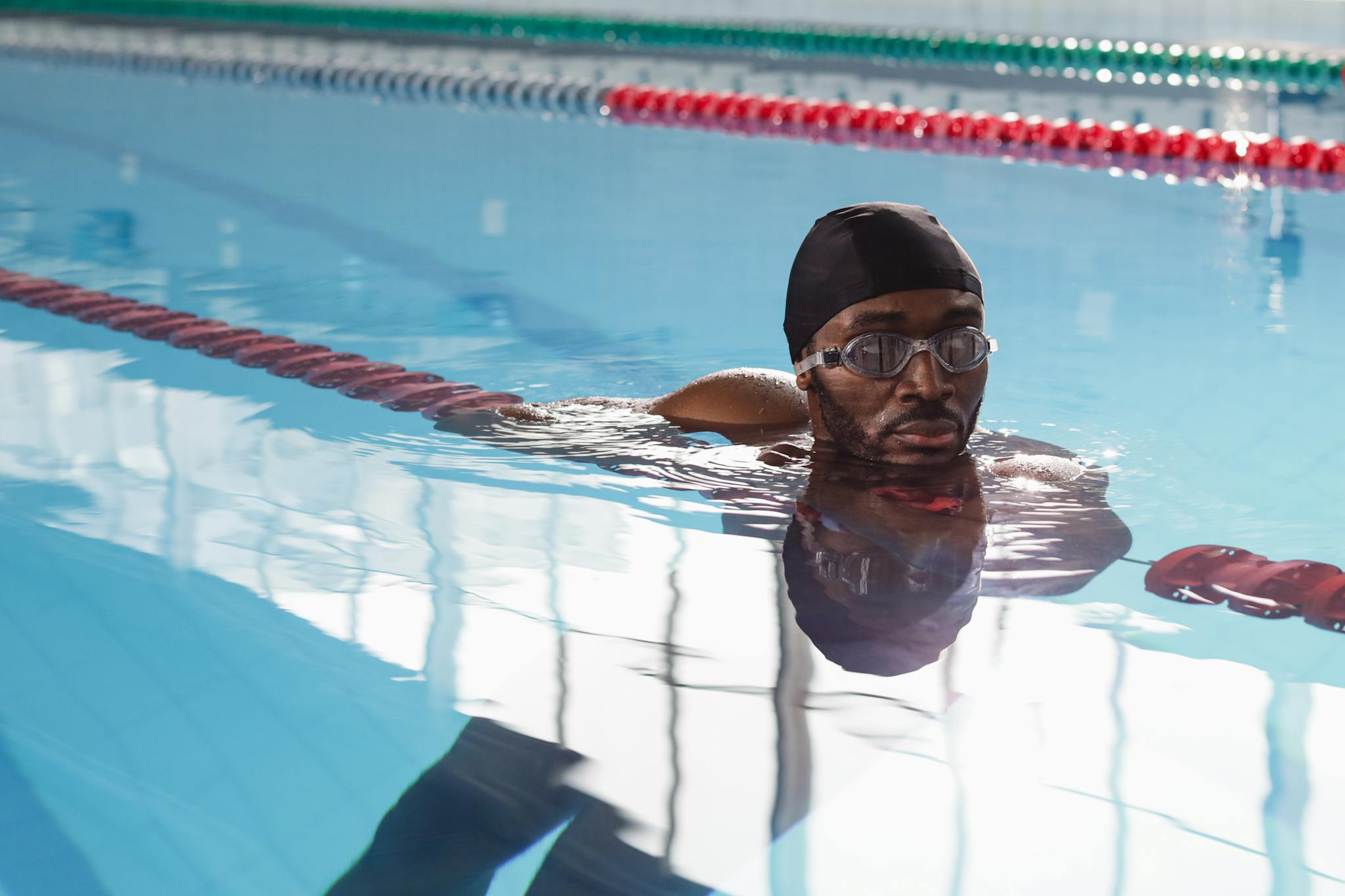 Close-up of a man swimming in an indoor pool, wearing a swim cap and goggles.